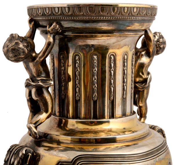 Grande vaso biansato in argento con prese a guisa di putti su foglie d'acanto a sorreggere l'orlo...