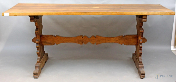 Tavolo di linea rettangolare in noce, poggiante su due gambe intagliate legate da traversa, cm h 82x197x71, XX secolo.