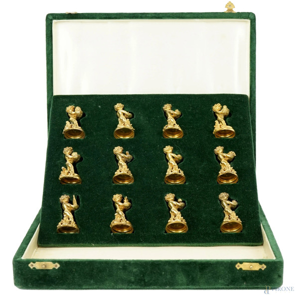 Dodici segnaposto in argento vermeille modellati come figure di putti con cesti, entro cofanetto originale in velluto verde, metà XX secolo, cm h 3,5, gr. 241