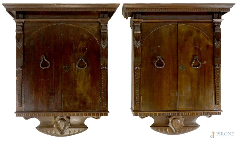 Coppia di armadietti pensili in noce, inizi XX secolo, cappello aggettante modanato e dentellato, fronte a due ante, fregio scolpito con scudetto, cm h 127x100x43, (difetti)  - Asta I TORNATA DI ASTA A TEMPO DI ARTE MODERNA E ANTIQUARIATO - Aste Pirone