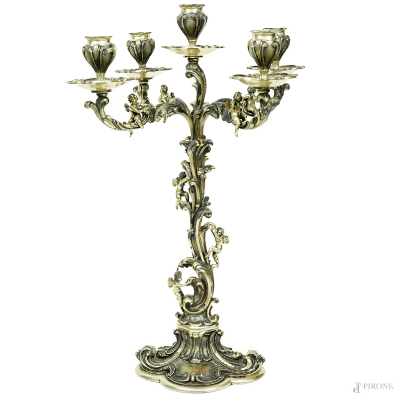 Candelabro in argento a cinque fiamme, bracci riccamente cesellati e sbalzati a volute, foglie e ricci con piccoli putti giocosi, seconda metà XX secolo, cm h 42x29, peso lordo gr. 2320 (appesantito).  - Asta ASTA A TEMPO DI ANTIQUARIATO E ARTE MODERNA - Aste Pirone