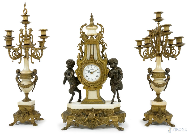 Trittico in bronzo e marmo, inizi XX secolo, orologio con corpo a lira affiancato da due satiri, quadrante smaltato a numeri romani, candelabri a sette fiamme con corpo a balaustro decorato da puttini e festoni, altezza max cm 69  - Asta ASTA A TEMPO - Aste Pirone